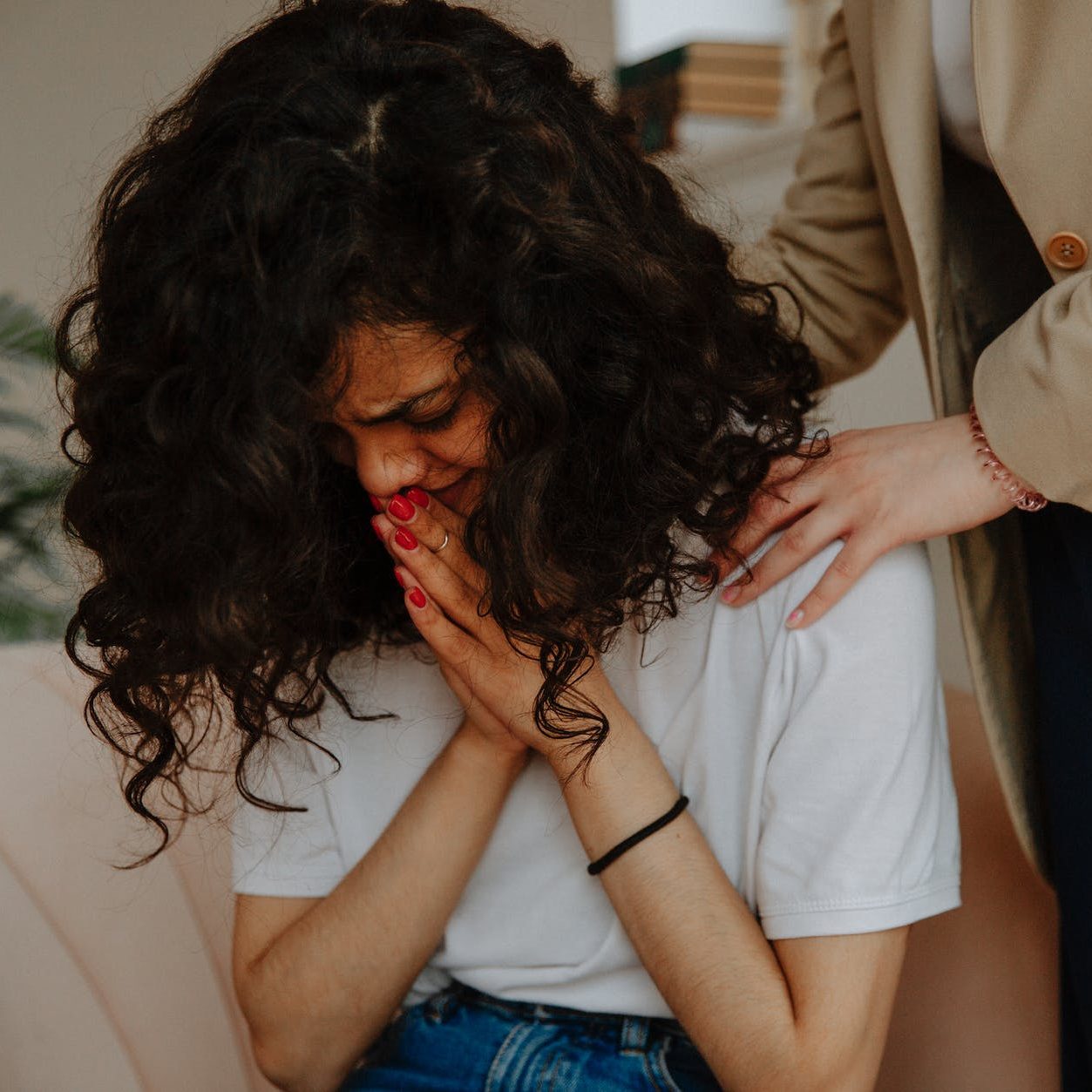 A woman crying, and someone has their hands on her shoulders to comfort her. (wallflowerhaze.com)