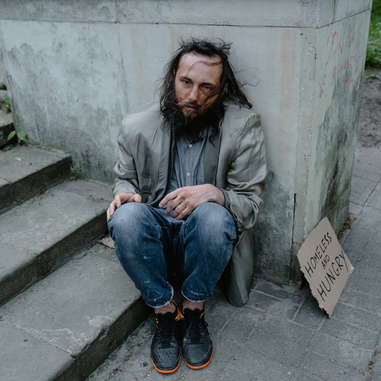 A stock photo of the stereotypical image of homeless man sitting on the street with a cardboard sign. (wallflowerhaze.com)