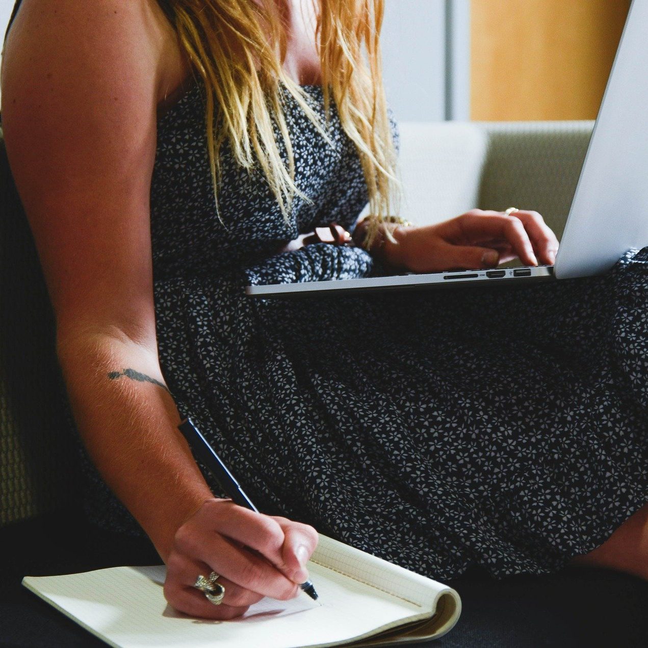 A woman with a laptop on her lap and a notepad next to her. She is writing on the notepad with a pen. 5 Ways To Find Inspiration For Your Mental Health Blog (wallflowerhaze.com)