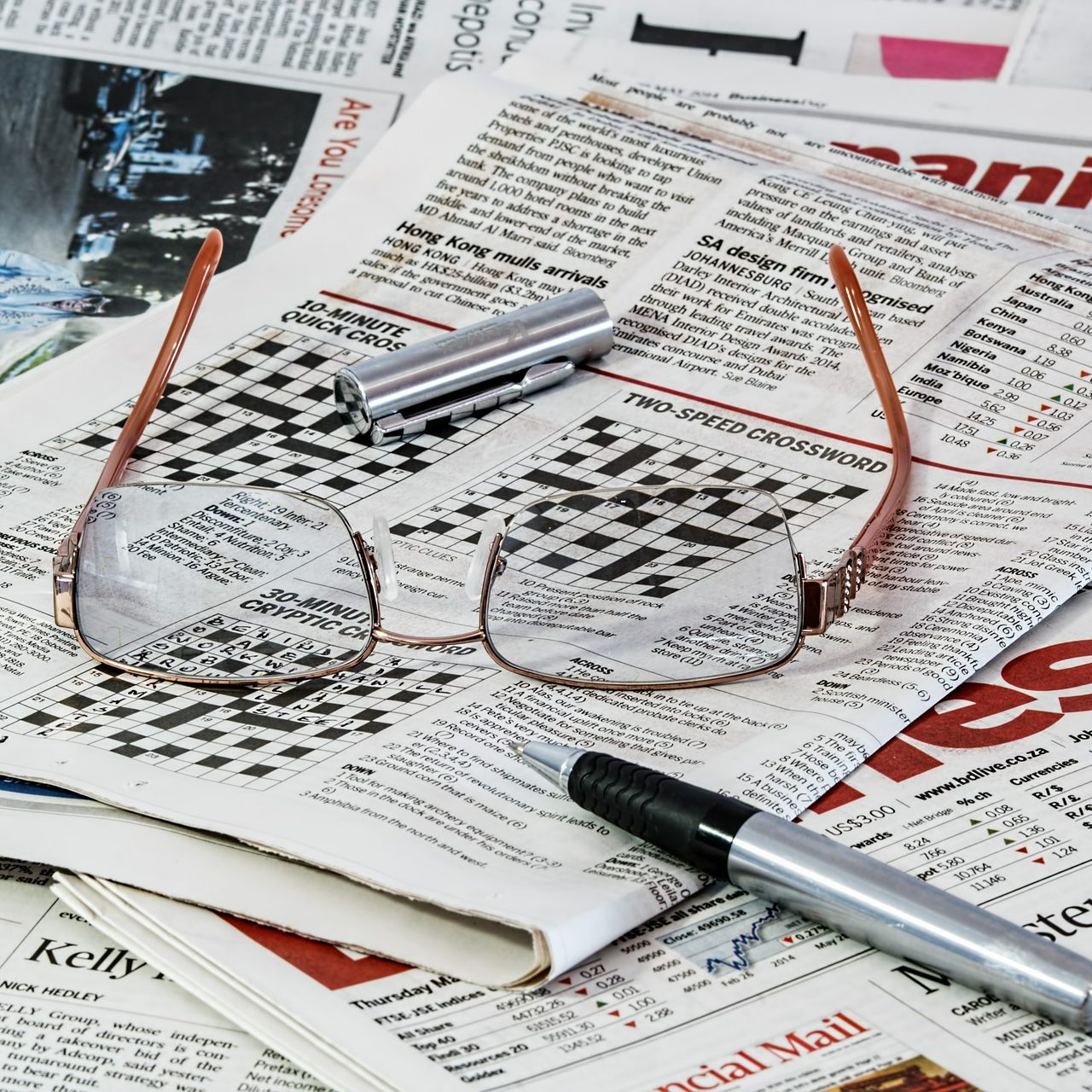 A pile of newspaper puzzles pages, with a pair of glasses and a pen. (wallflowerhaze.com)