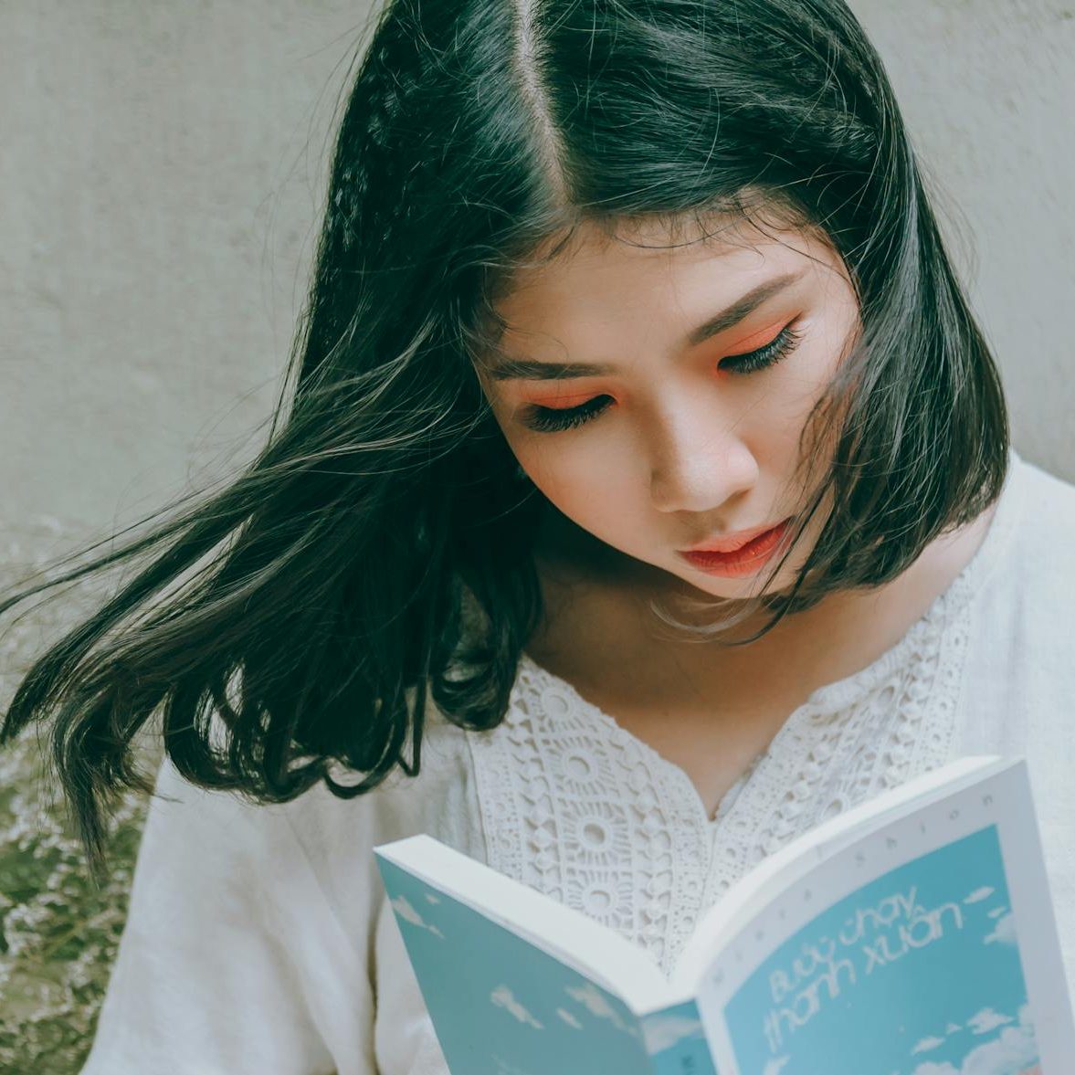 A woman looking down at an open book. (wallflowerhaze.com)