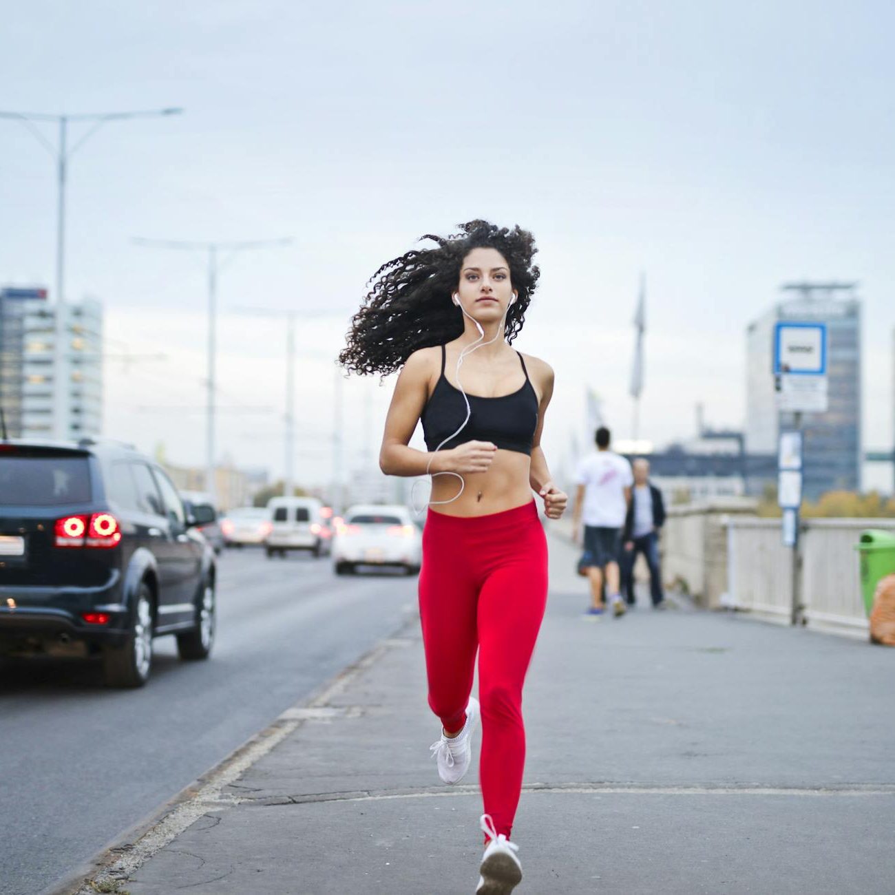 A woman in running gear, wearing earphones and running down the street, towards the camera. Her hair is flowing in the wind and her gaze is set ahead. (wallflowerhaze.com)