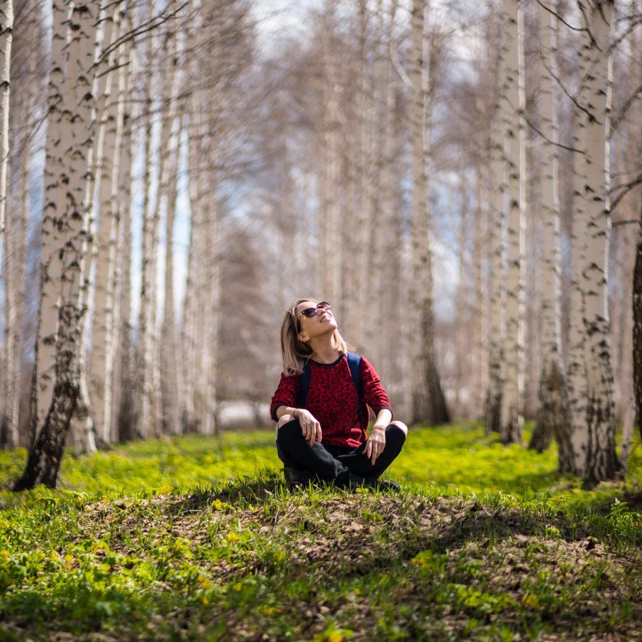 A woman sitting cross-legged in a forest, looking up at the sky and smiling. What Recovery Looks Like To Me (wallflowerhaze.com)