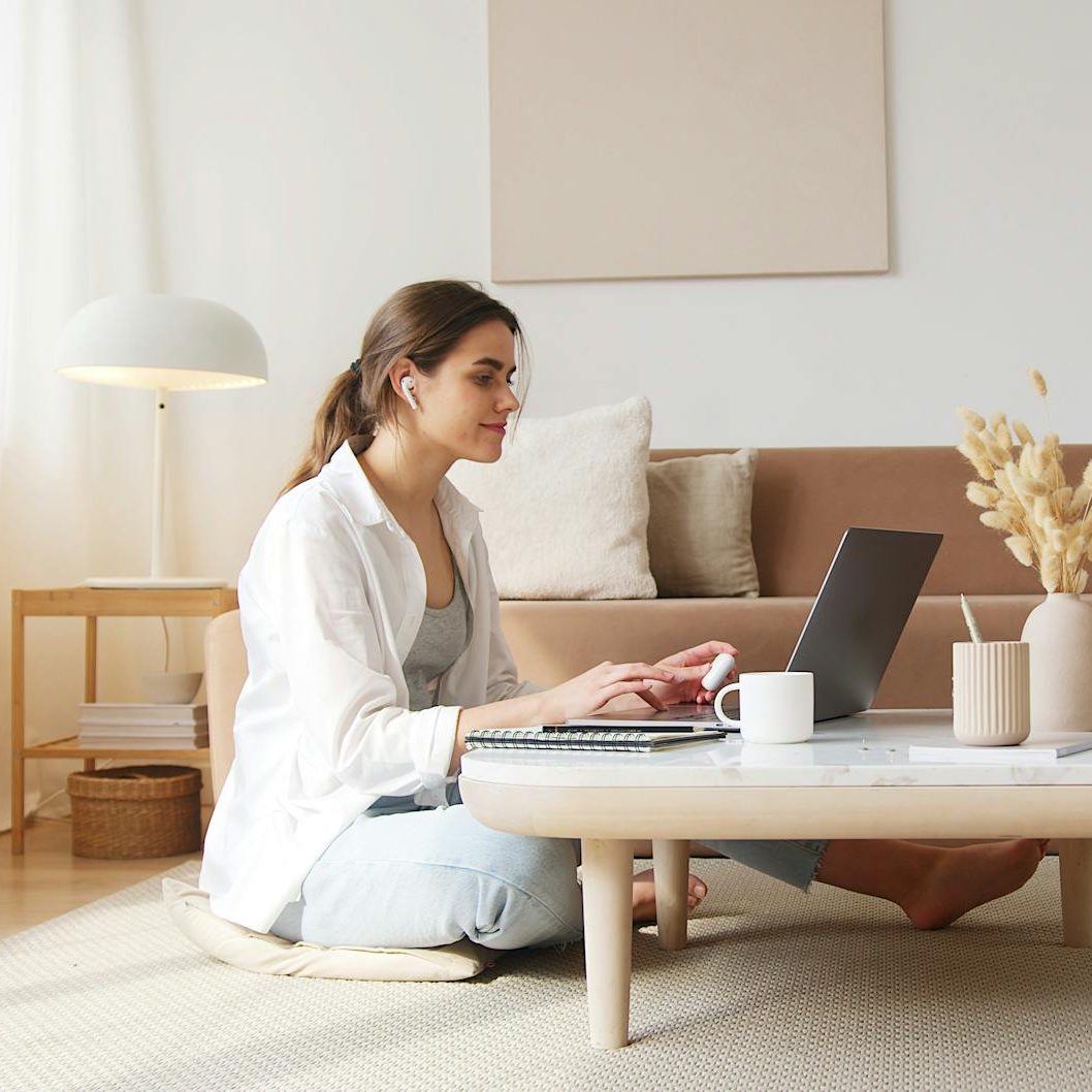 A woman sitting on the floor with her laptop on a coffee table. She is watching the screen and wearing earphones. (wallflowerhaze.com)