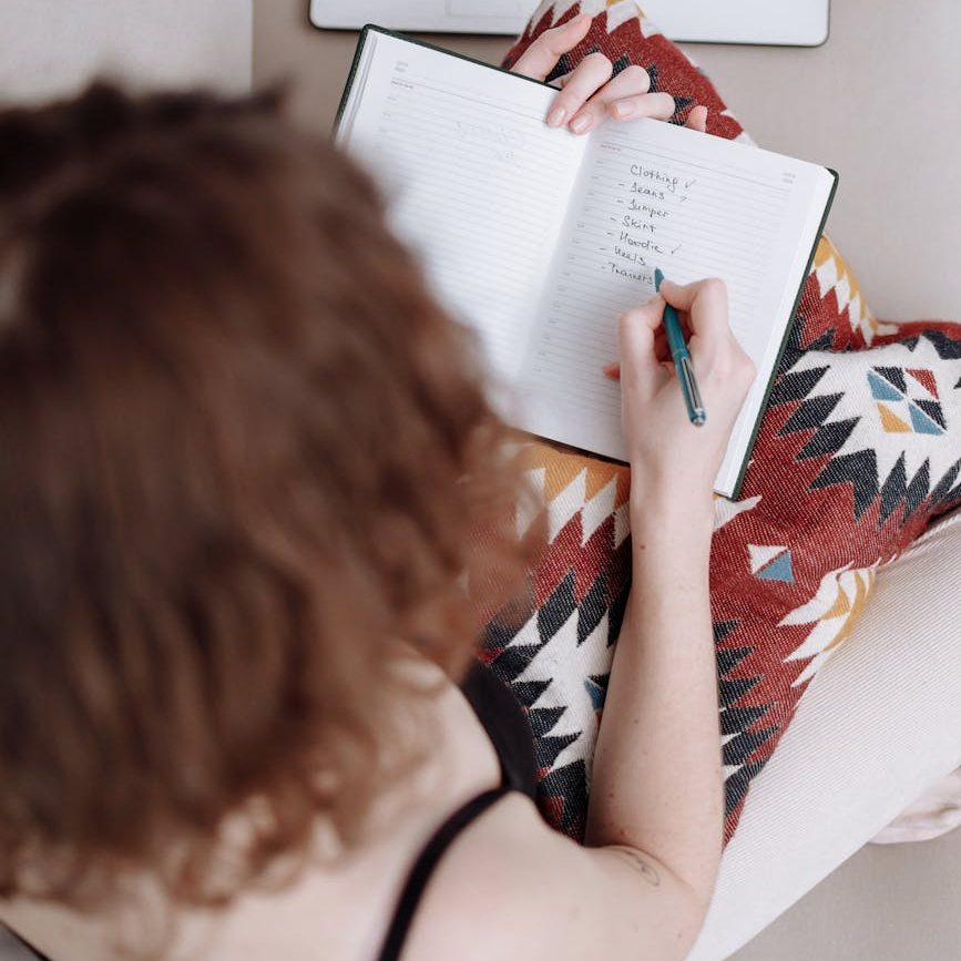 Looking over the shoulder of a woman who is writing a list in a notebook.