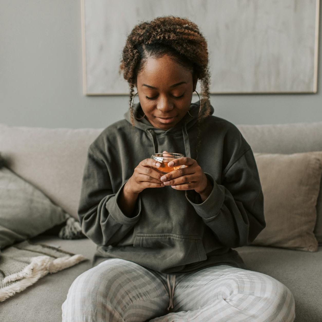 A woman looking down at the glass cup of tea in her hands. She is smiling and wearing comfortable clothes. (wallflowerhaze.com)