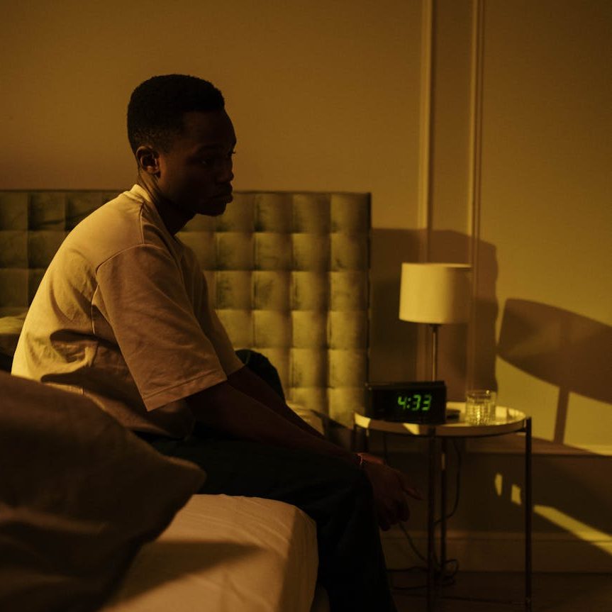 A man sitting on his bed, staring into space. The clock shows is it around 4am. (wallflowerhaze.com)