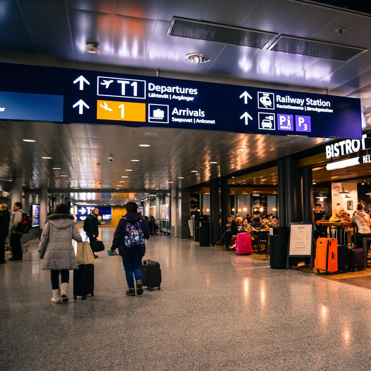 Stock photo of inside an airport, people walking with suitcases, departures and arrivals signs, a café. (wallflowerhaze.com)
